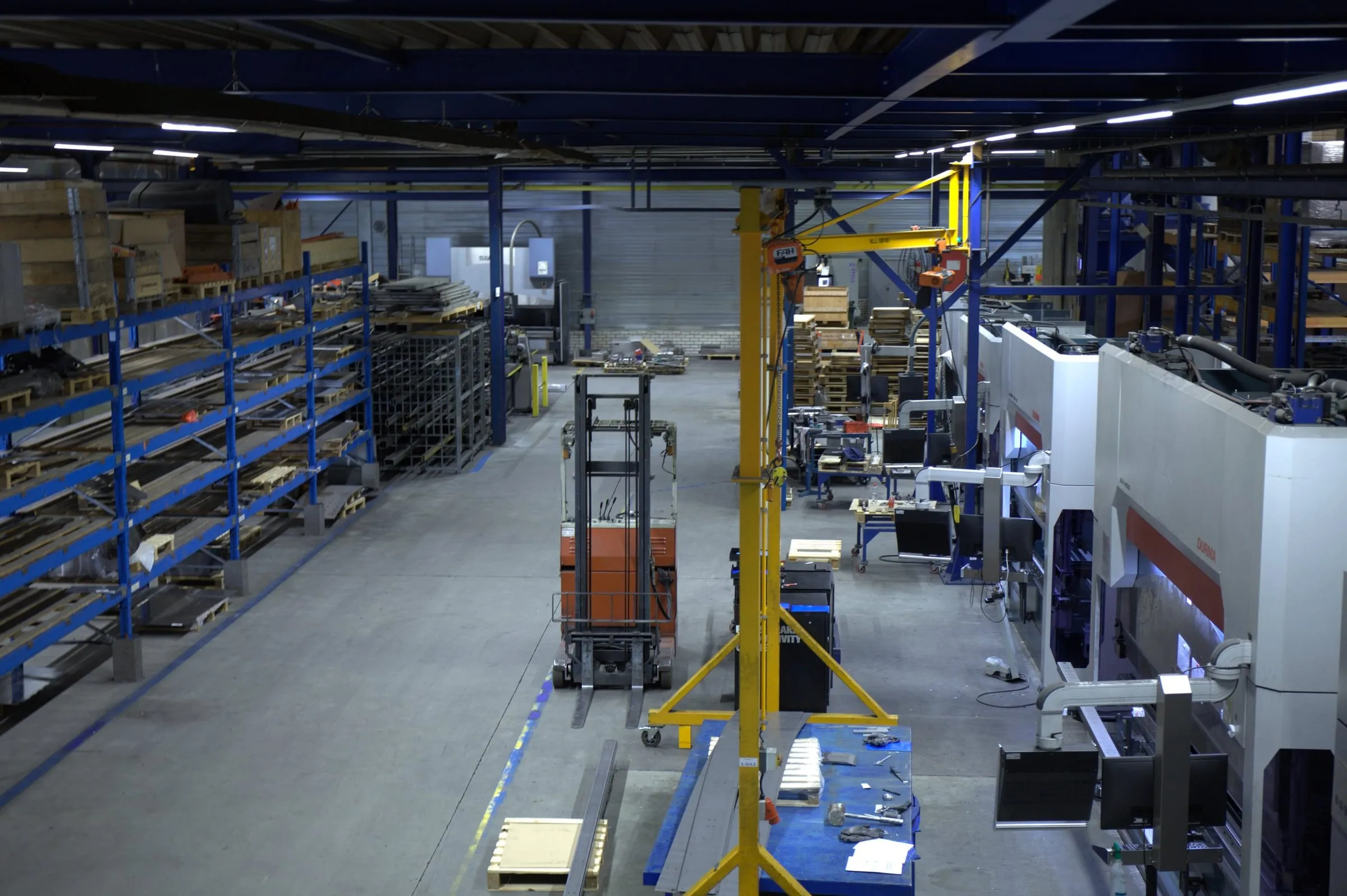 Blik vanaf hoogte over de productiehal, met de rij kantbanken en de stellingen met materiaal